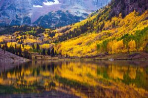 fall colors of yellow and orange trees reflect on the water with mountain in background Tivoli Lodge Vail Colorado