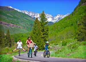 family of four enjoy their bike ride along a path with mountains in background Tivoli Lodge Vail Colorado
