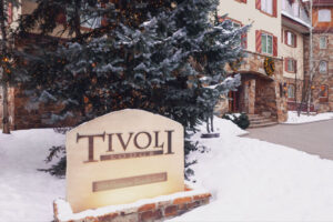 outdoor view of Tivoli Lodge Vail Colorado with stone sign, large lit tree, and stone entrance during winter time