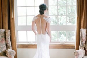 bride wearing open back dress with row of buttons looks out the window Tivoli Lodge Vail Colorado